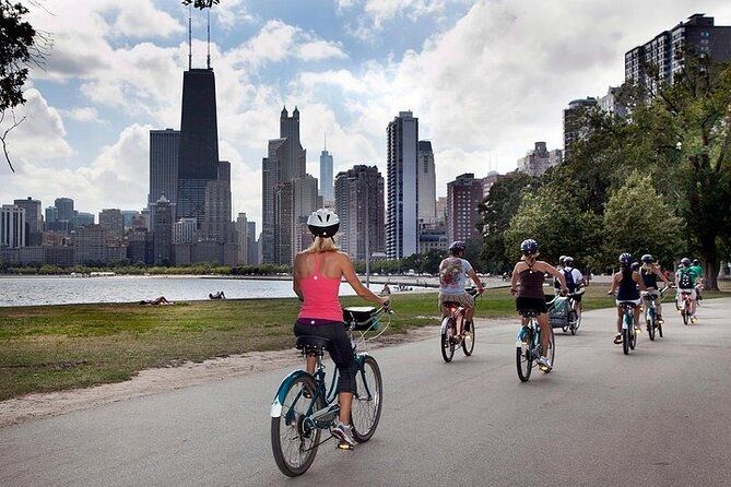 A group of people are riding bicycles down a path in front of a city skyline.