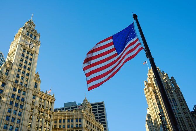 An american flag is flying in front of a clock tower in a city.