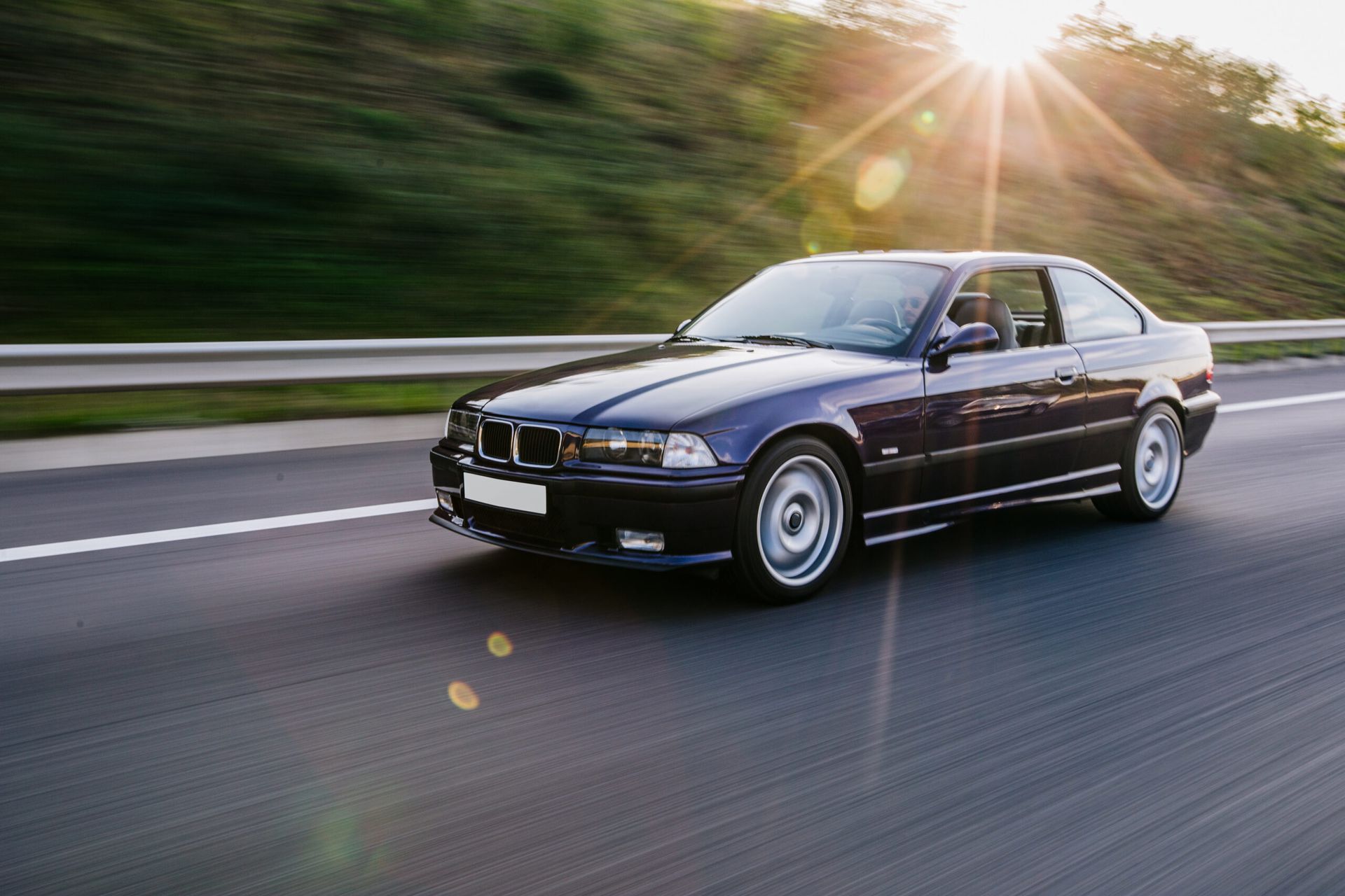 A blue car is driving down a highway with the sun shining through the windshield.
