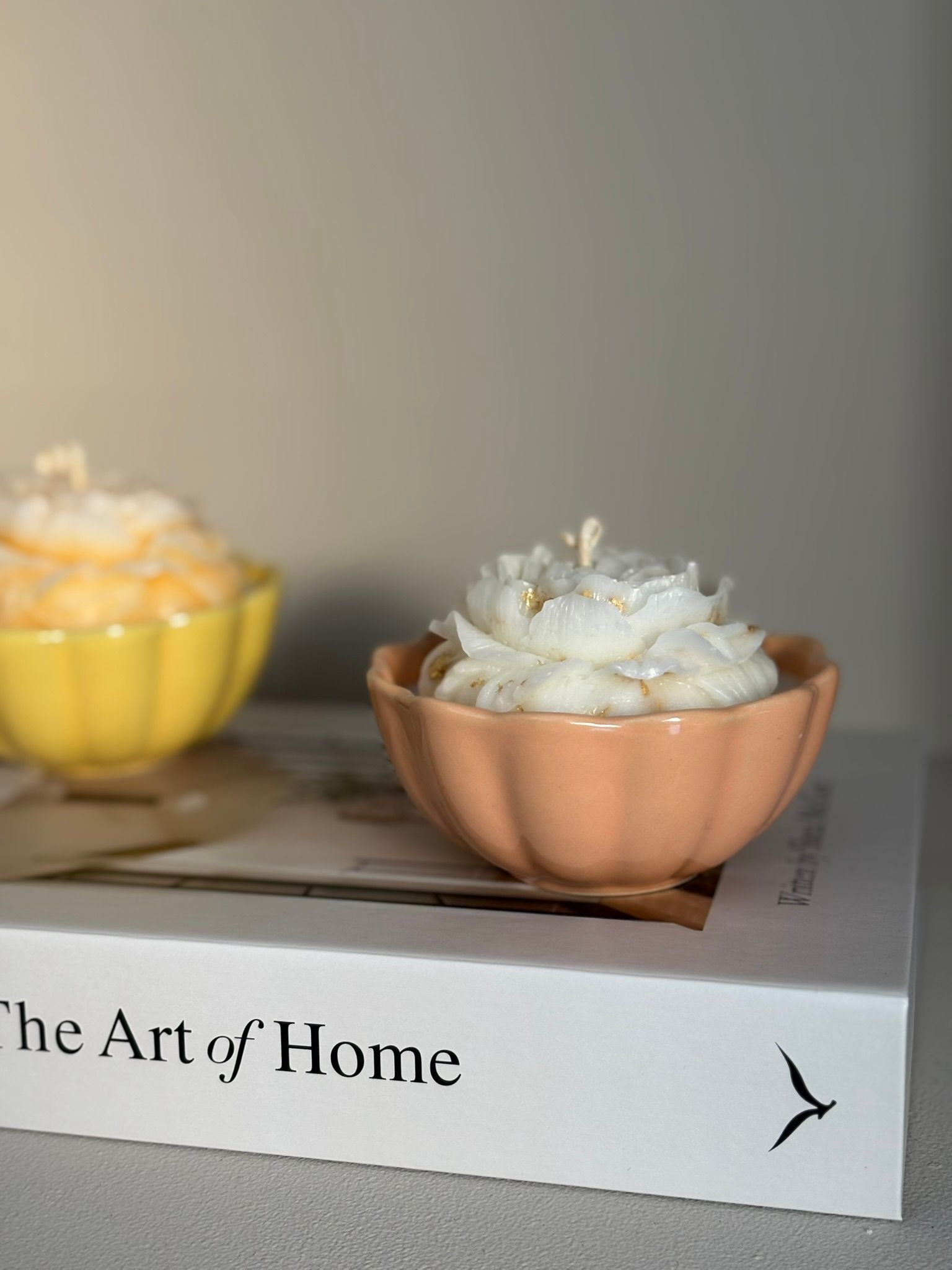 Twee bloemvormige kaarsen in perzik- en gele schalen bovenop een boek met de titel 