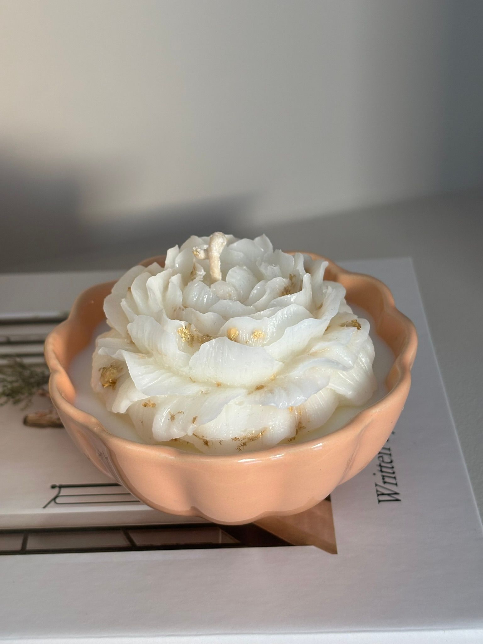 Twee bloemvormige kaarsen in perzik- en gele schalen bovenop een boek met de titel 