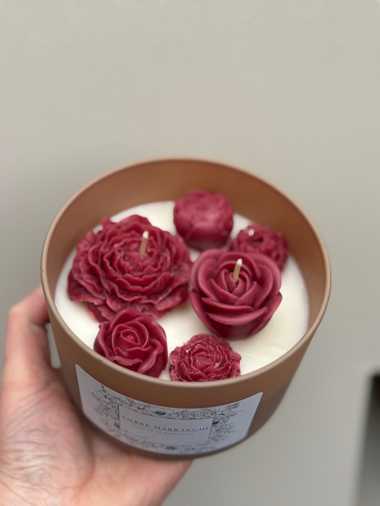 Een kaars in een bruine houder met daarin drie rode, bloemvormige kaarsen, op een stapel boeken.