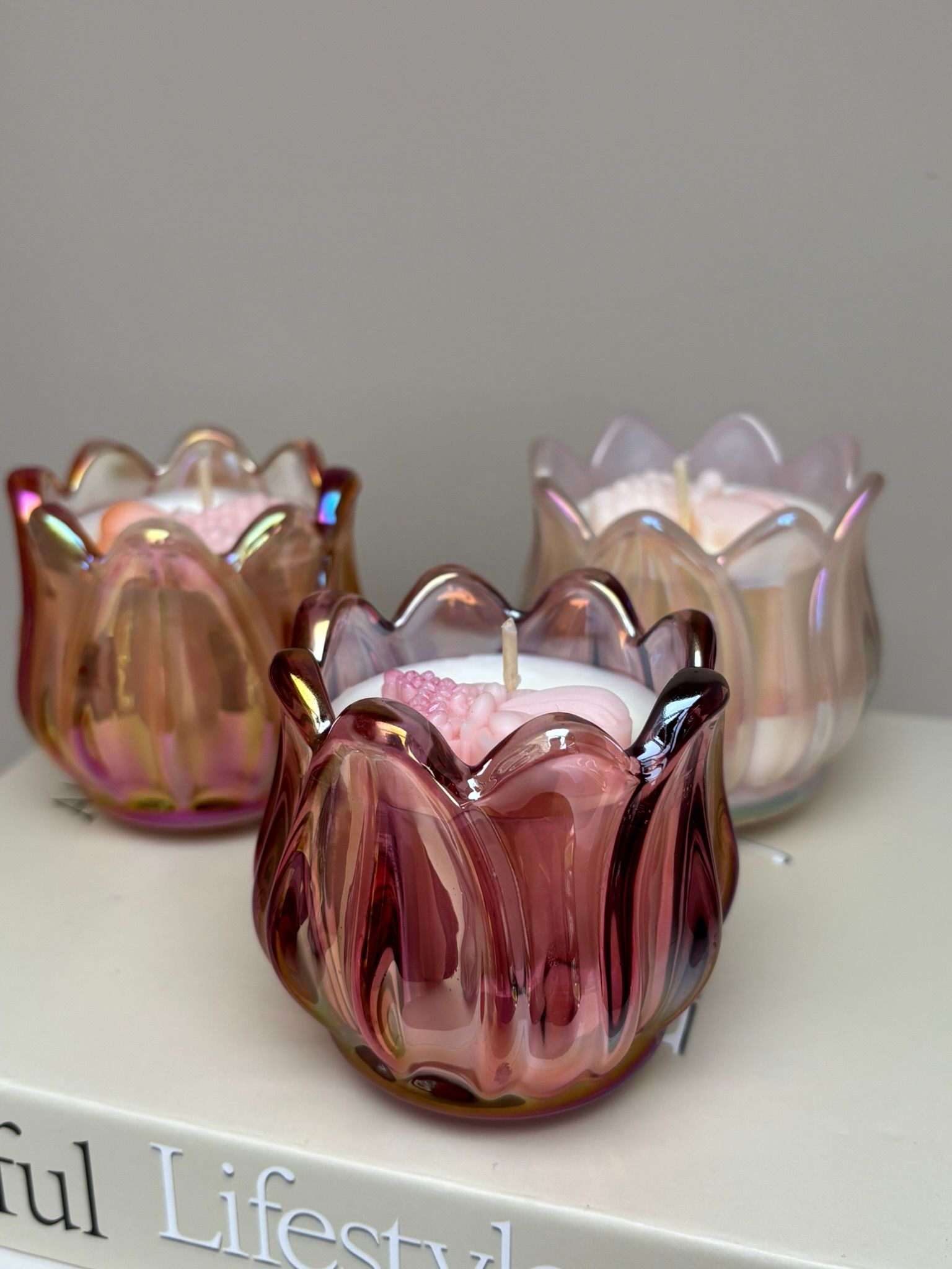 Drie tulpvormige kaarsen van iriserend roze glas staan ​​op een boek.