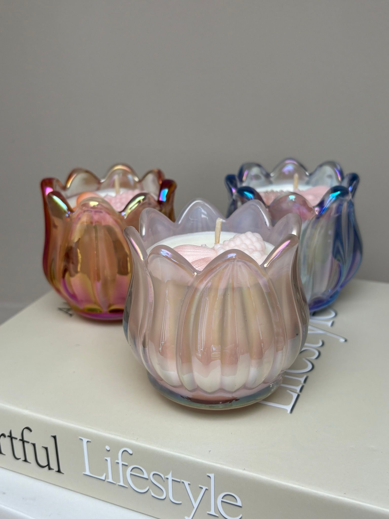 Drie tulpvormige, iriserende glazen kaarsen bovenop een boek met 'Artful Lifestyle' op de rug.