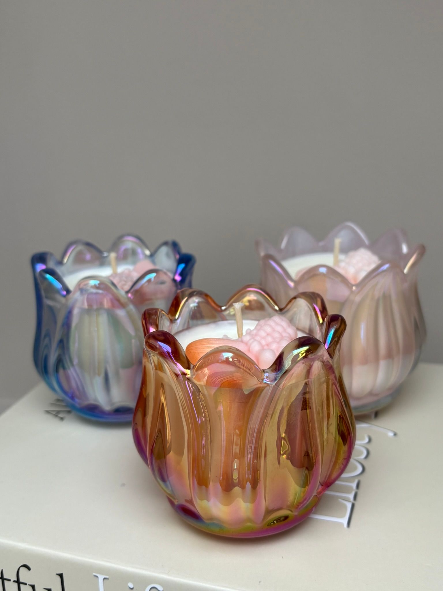 Drie iriserende, tulpvormige kandelaars met brandende witte kaarsen en decoratieve kristallen.