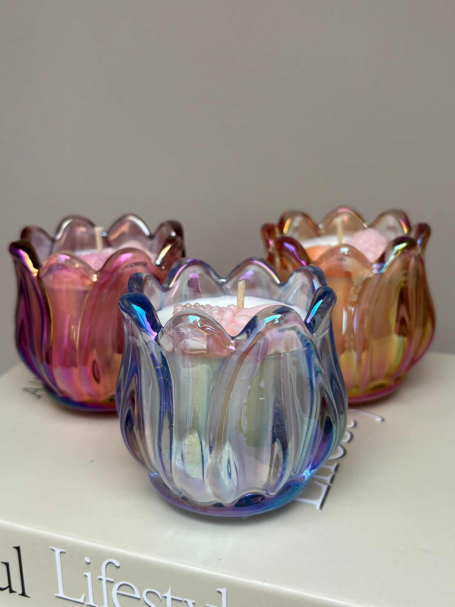 Drie iriserende, tulpvormige kandelaars met brandende roze kaarsen op een boek.