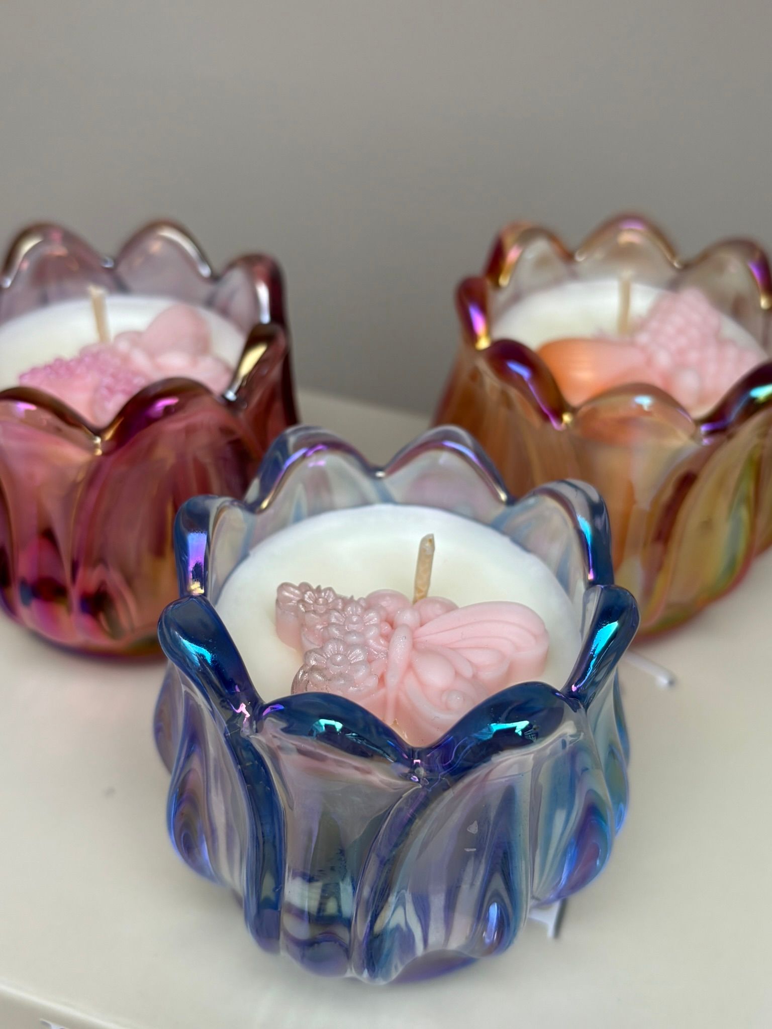 Drie iriserende, tulpvormige kandelaars met brandende roze kaarsen op een boek.