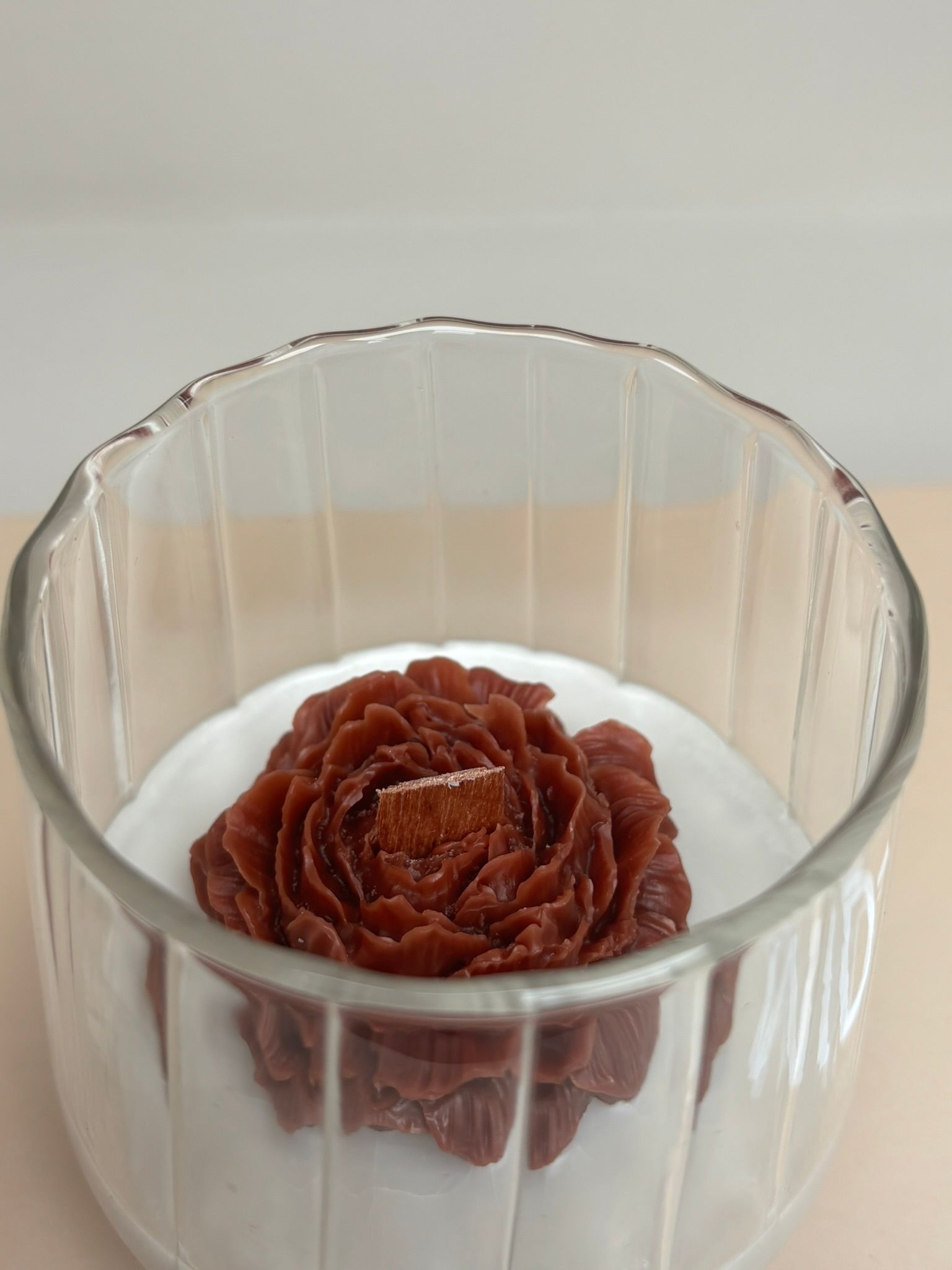 Glazen pot met een bruine bloemsculptuur op een witte voet, die rust op een beige boek.