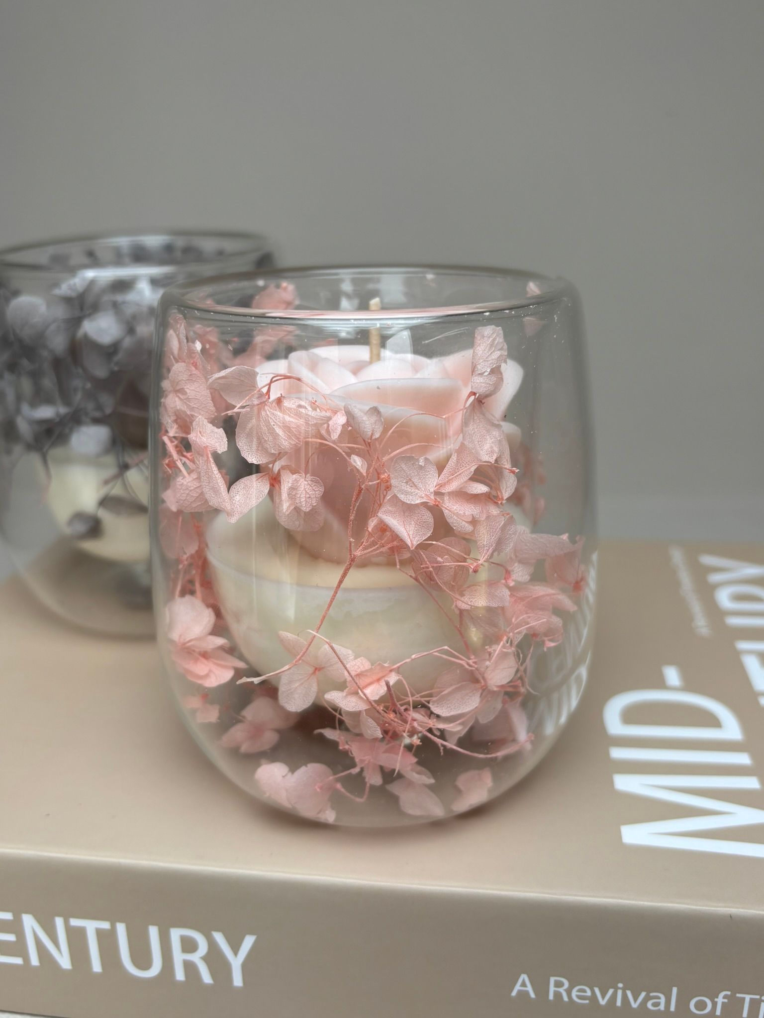 Doorzichtige glazen kaarsenstandaards met roze bloemen en kaarsen erin, die op een boek staan.