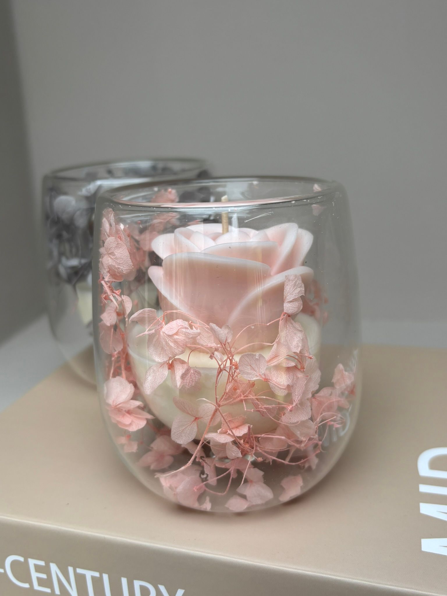 Doorzichtige glazen kaarsenstandaards met roze bloemen en kaarsen erin, die op een boek staan.