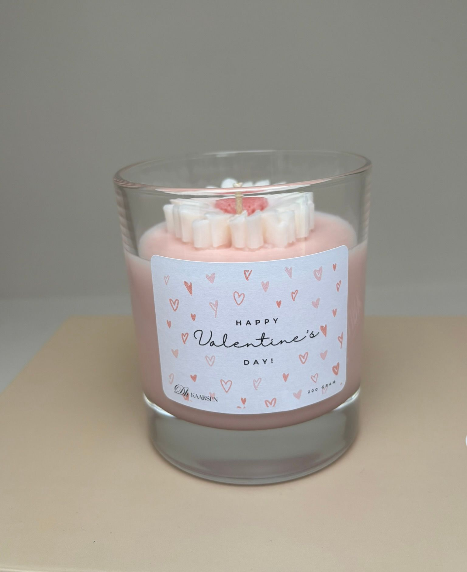 Roze kaars in een glazen pot met een Valentijnsdag-etiket, afgewerkt met decoratieve was.
