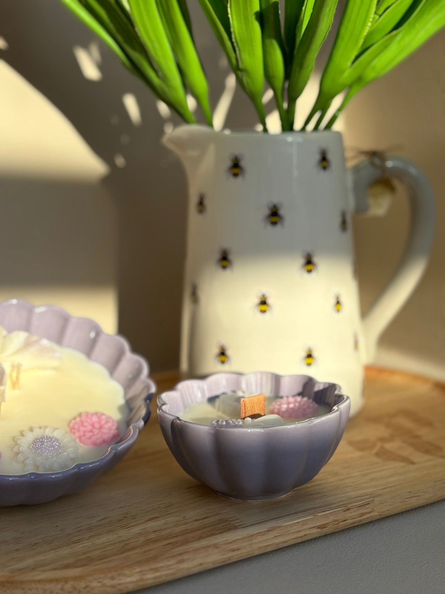 Een paarse, bloemvormige kaarsenhouder met witte was, een houten lont en decoratieve wasversieringen in de vorm van bloemen en vlinders.