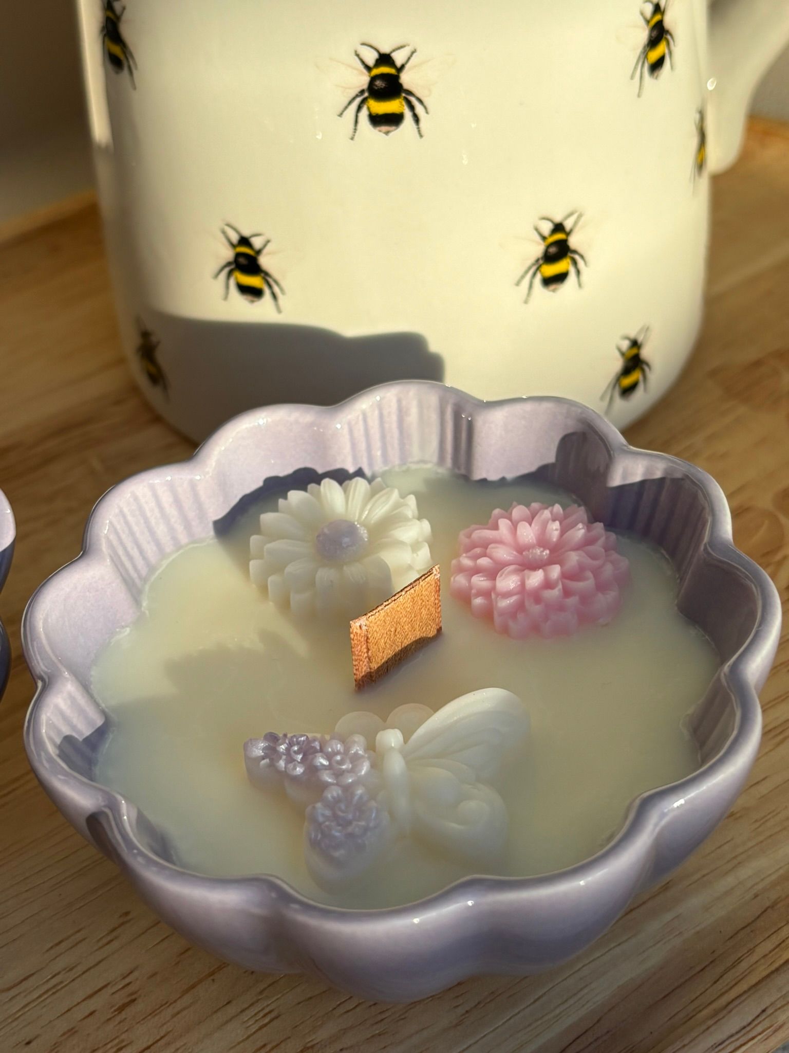 Een paarse, bloemvormige kaarsenhouder met witte was, een houten lont en decoratieve wasversieringen in de vorm van bloemen en vlinders.