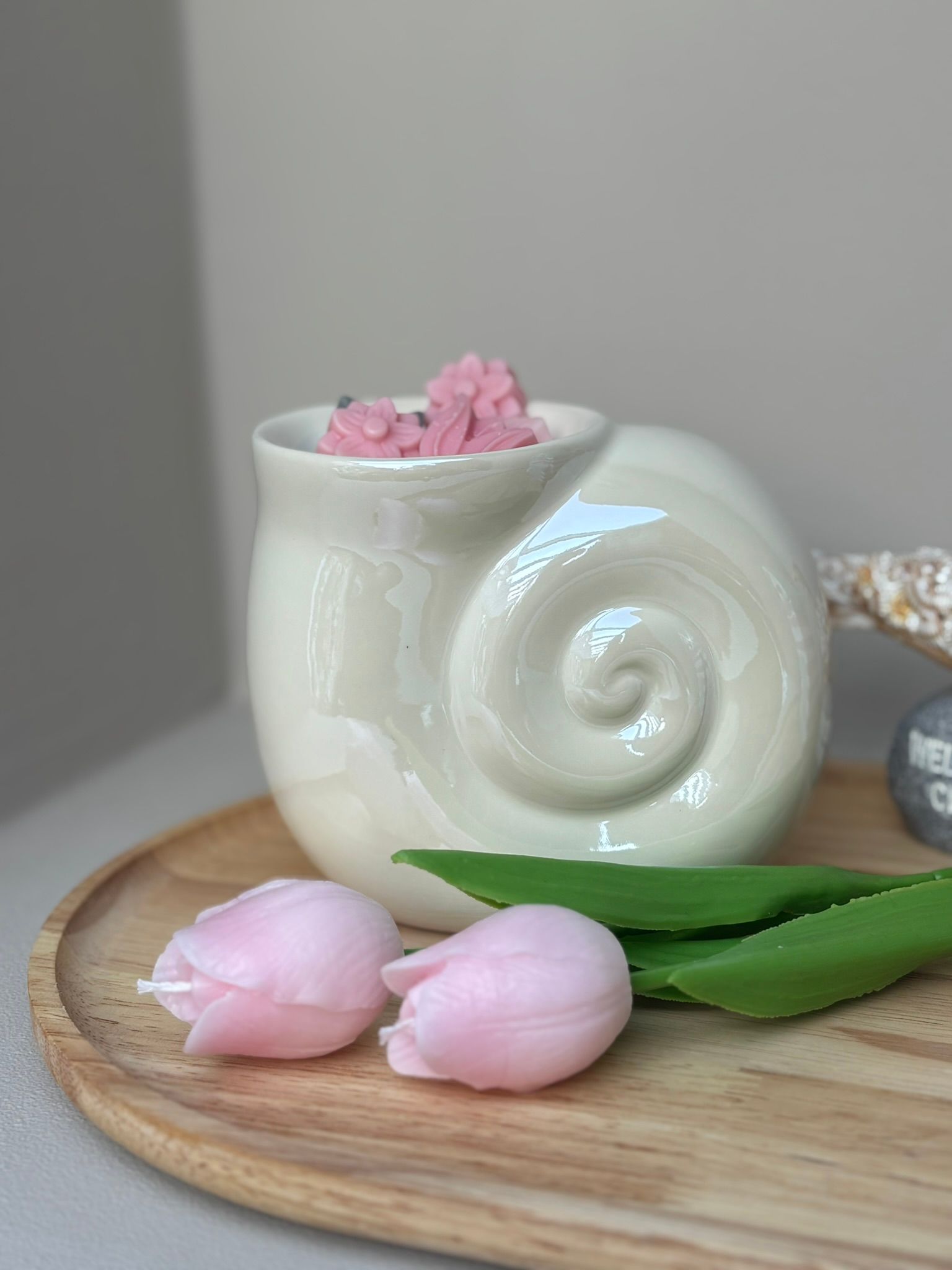 Een witte, slakvormige keramische waxbrander met daarin verschillende kleine, roze, bloemvormige waxblokjes.