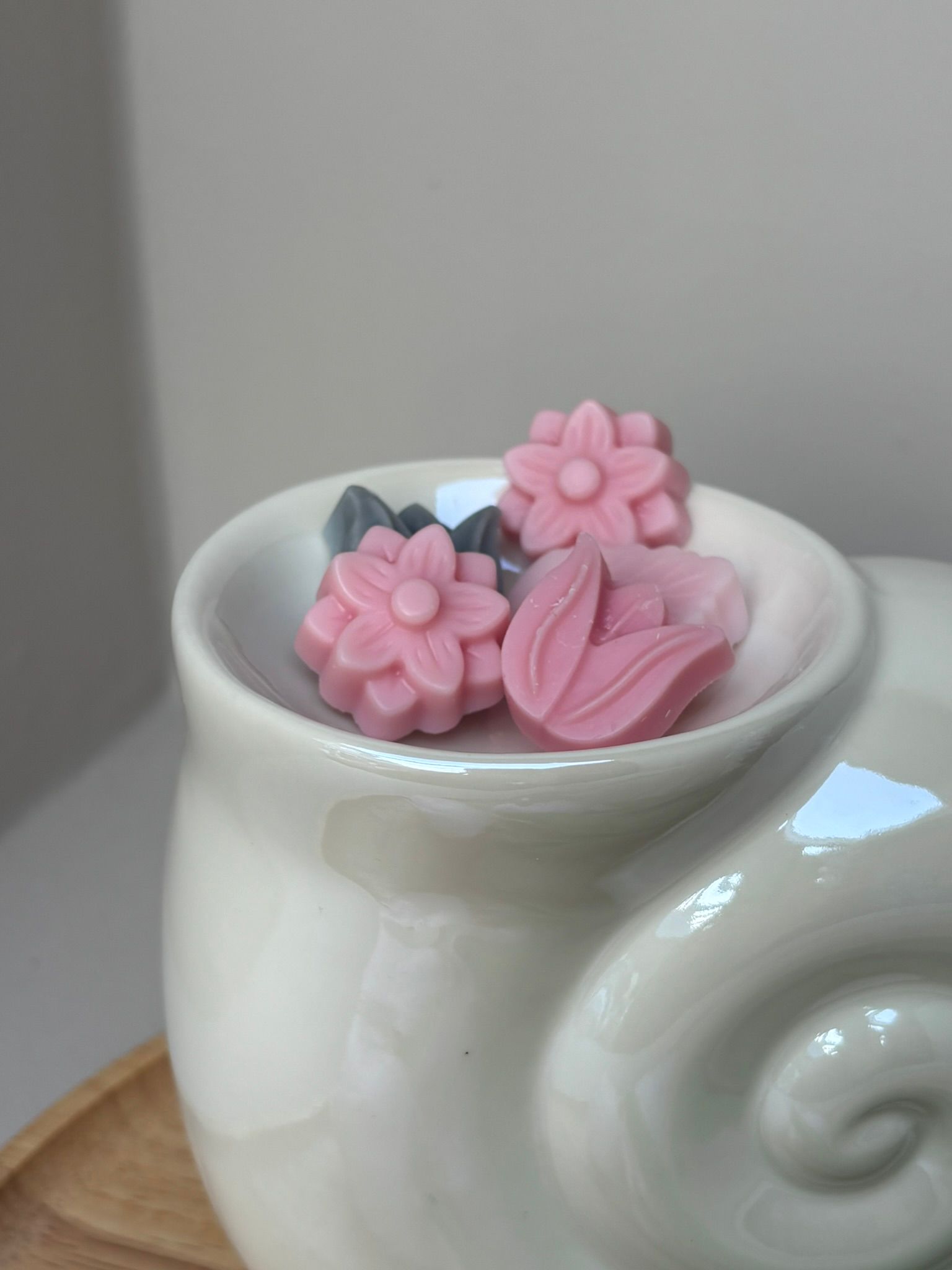 Een witte, slakvormige keramische waxbrander met daarin verschillende kleine, roze, bloemvormige waxblokjes.