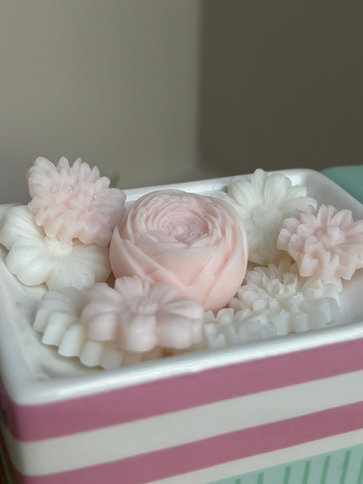 Een schaal gevuld met kleine, decoratieve wasbloemen in lichtroze en witte tinten.