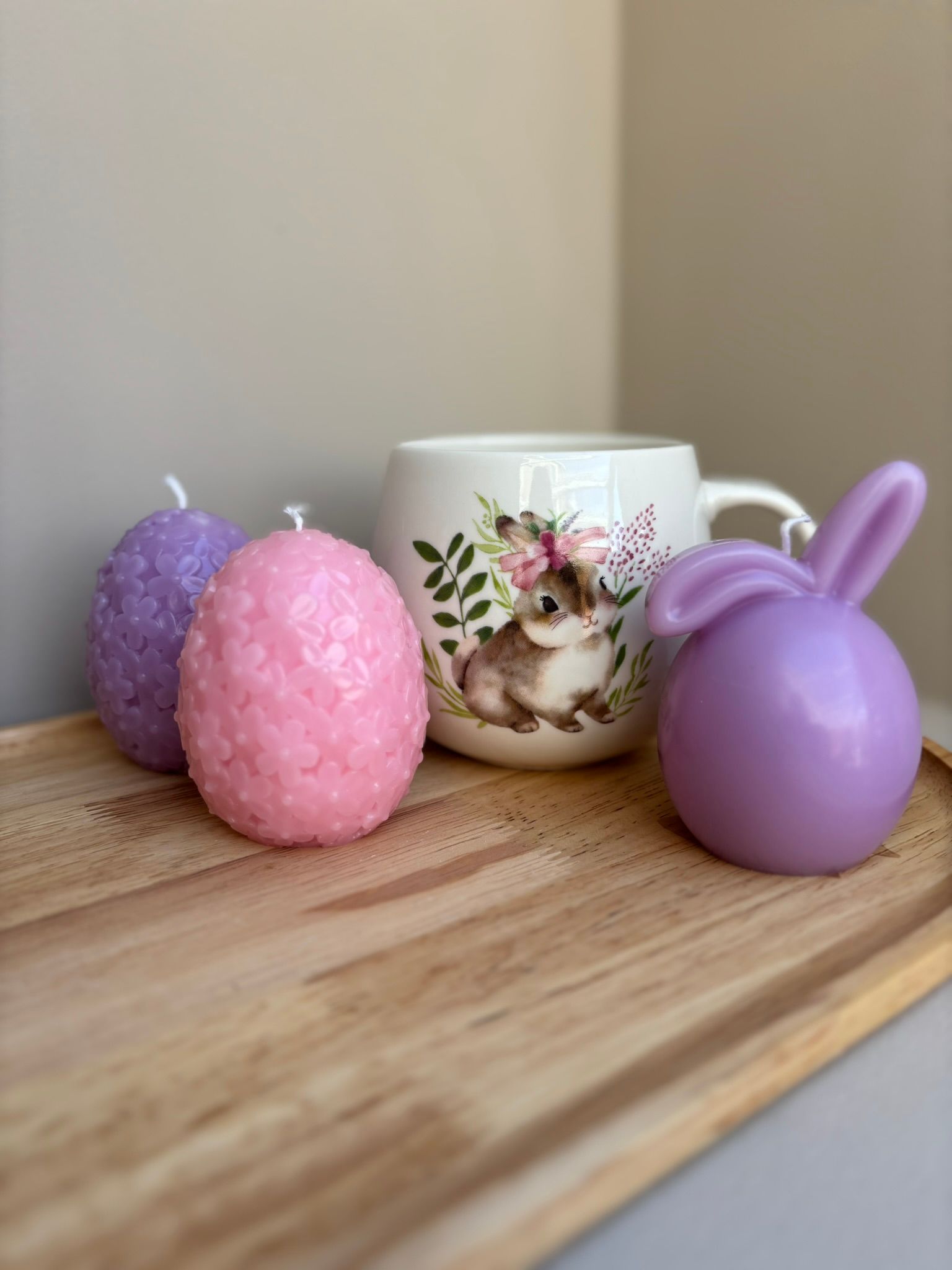 Drie decoraties met konijntjesthema: een konijntje van vilt, een paarse kaars en een roze kaars op een houten dienblad.