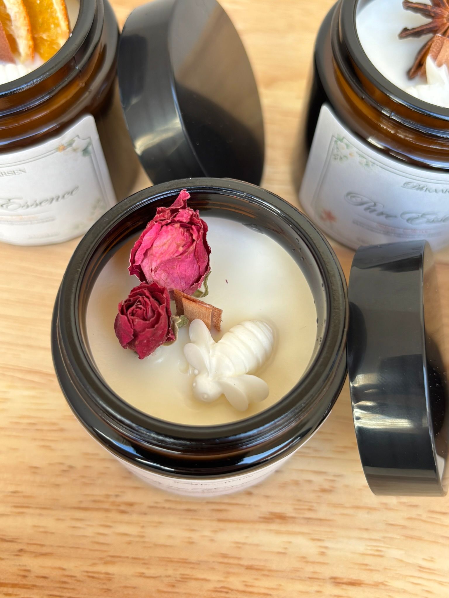 Kleine amberkleurige glazen potjes gevuld met kaarsen, afgewerkt met gedroogde bloemen, staan ​​op een houten plank.