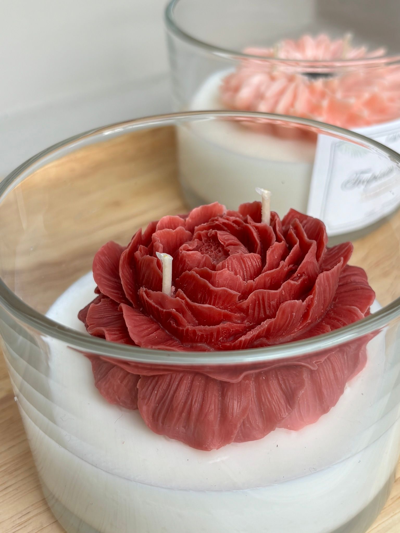 Twee kleine glazen kaarsen met witte was en roze bloemversieringen op een houten dienblad.