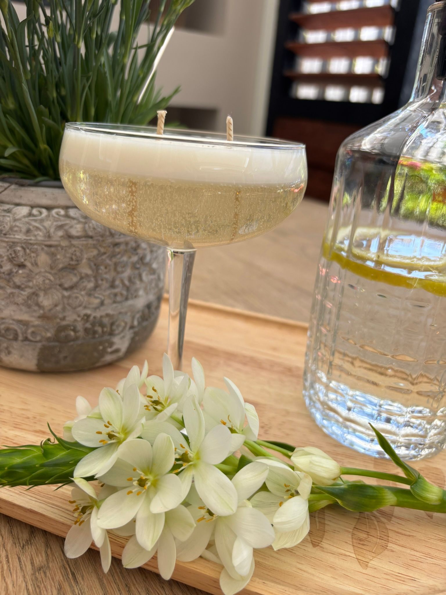 Een witte cocktail in een coupeglas, naast witte bloemen en een fles water op een tafel.