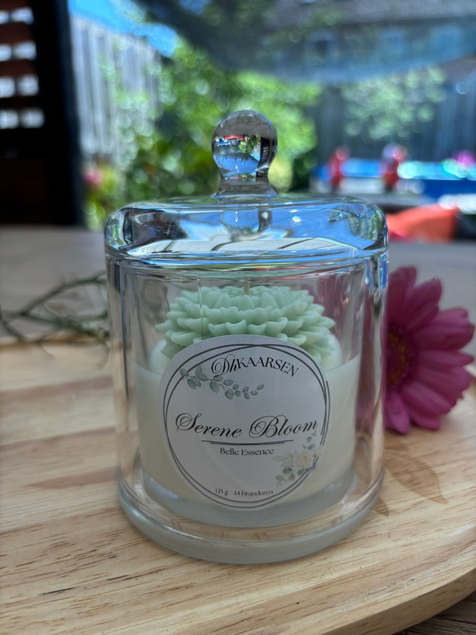Klein glazen kaarsenpotje met pastelgroene was op een houten dienblad buiten in de zon.