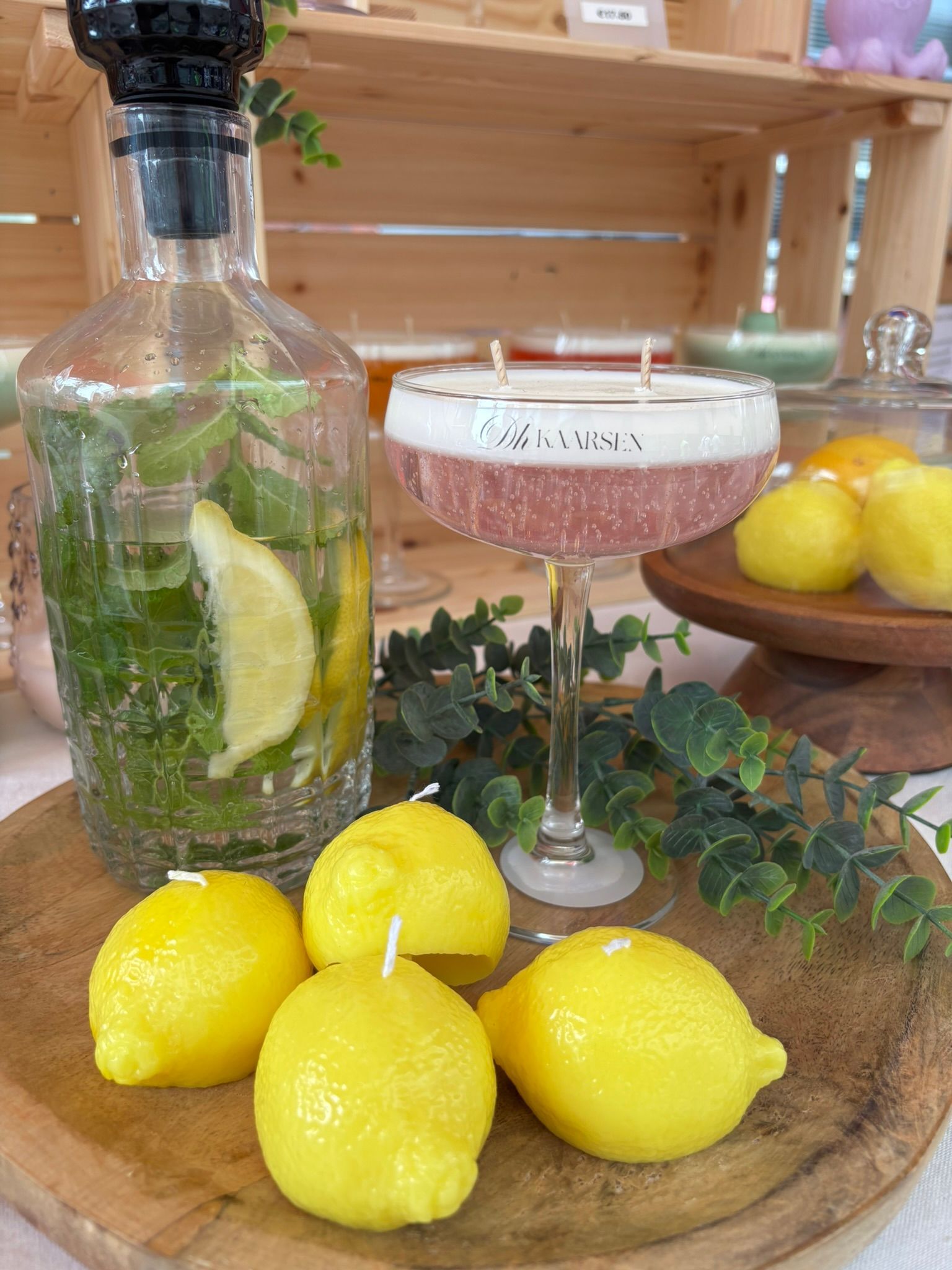 Cocktail met komkommer- en citroengarnituur naast heldere citroenen op een houten tafel.