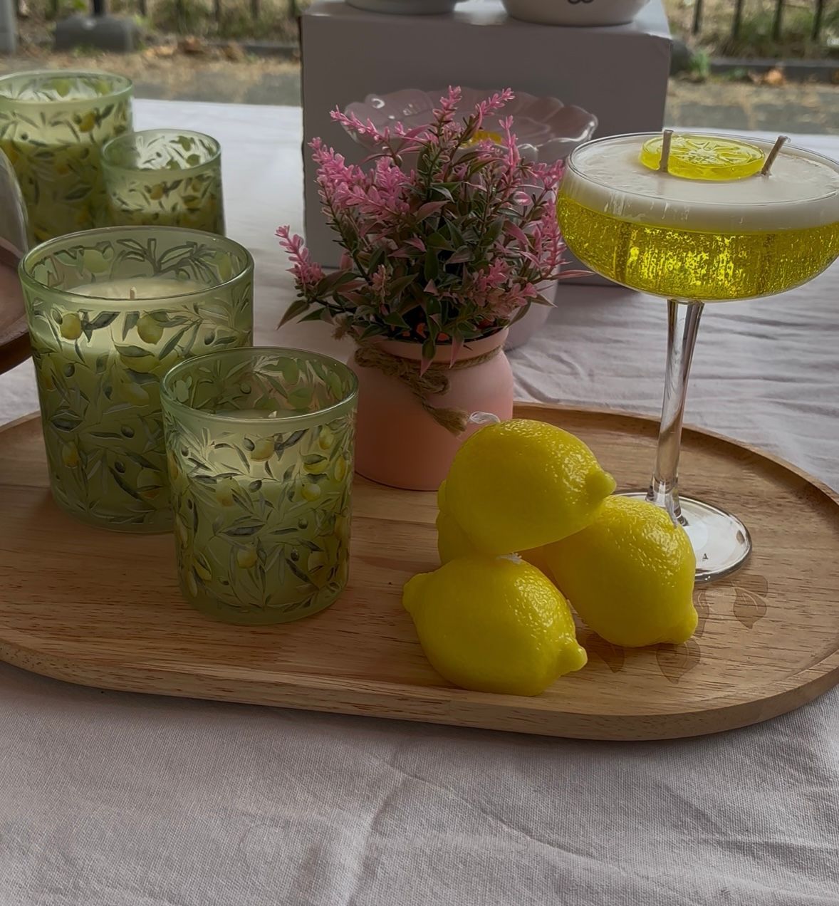Een dienblad met groene drankjes, citroengarnituur en een roze bloemstuk op tafel.