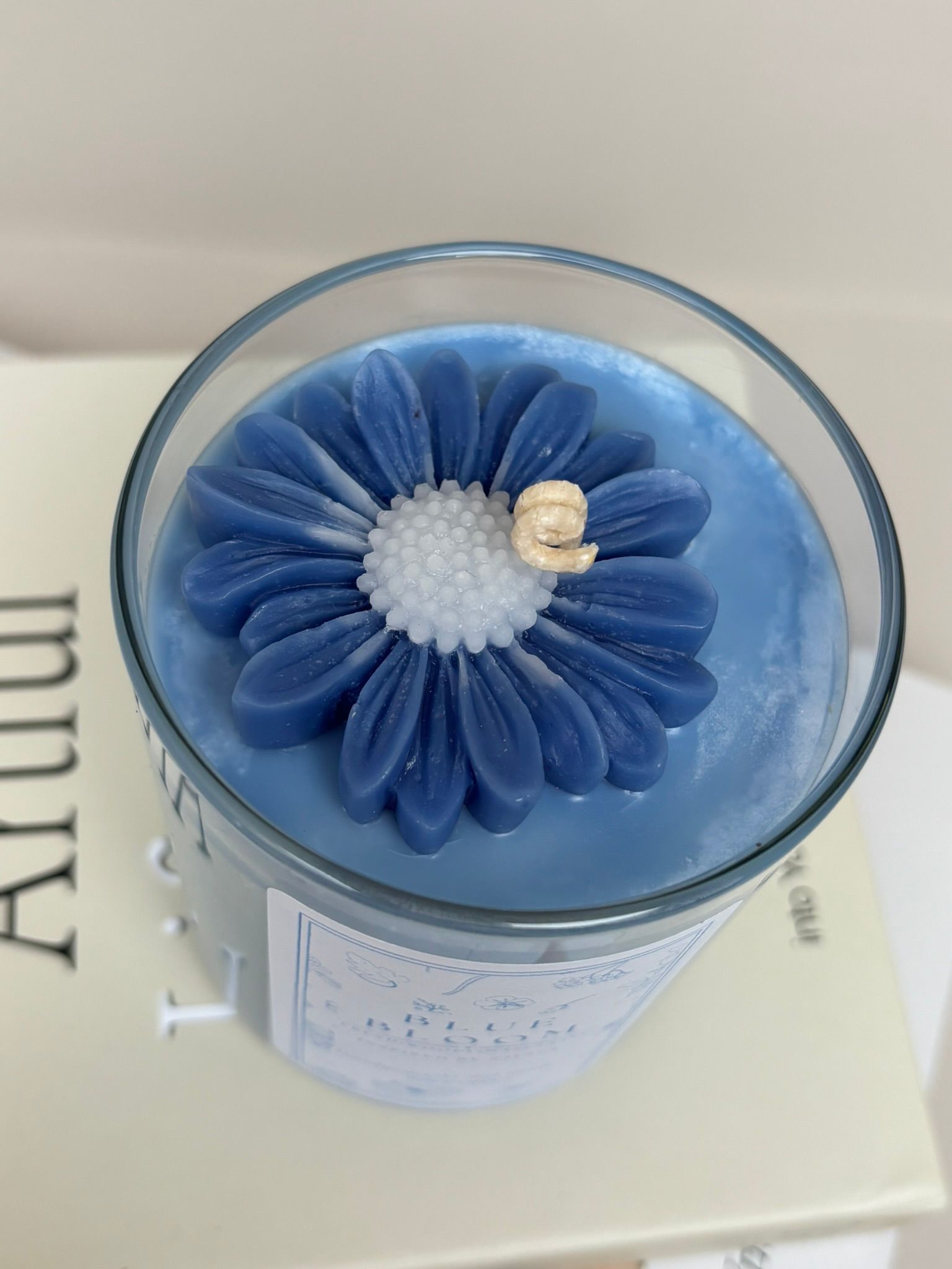 Een blauwe, bloemvormige kaars in een doorzichtige glazen houder, die op een lichtgekleurd boek staat.