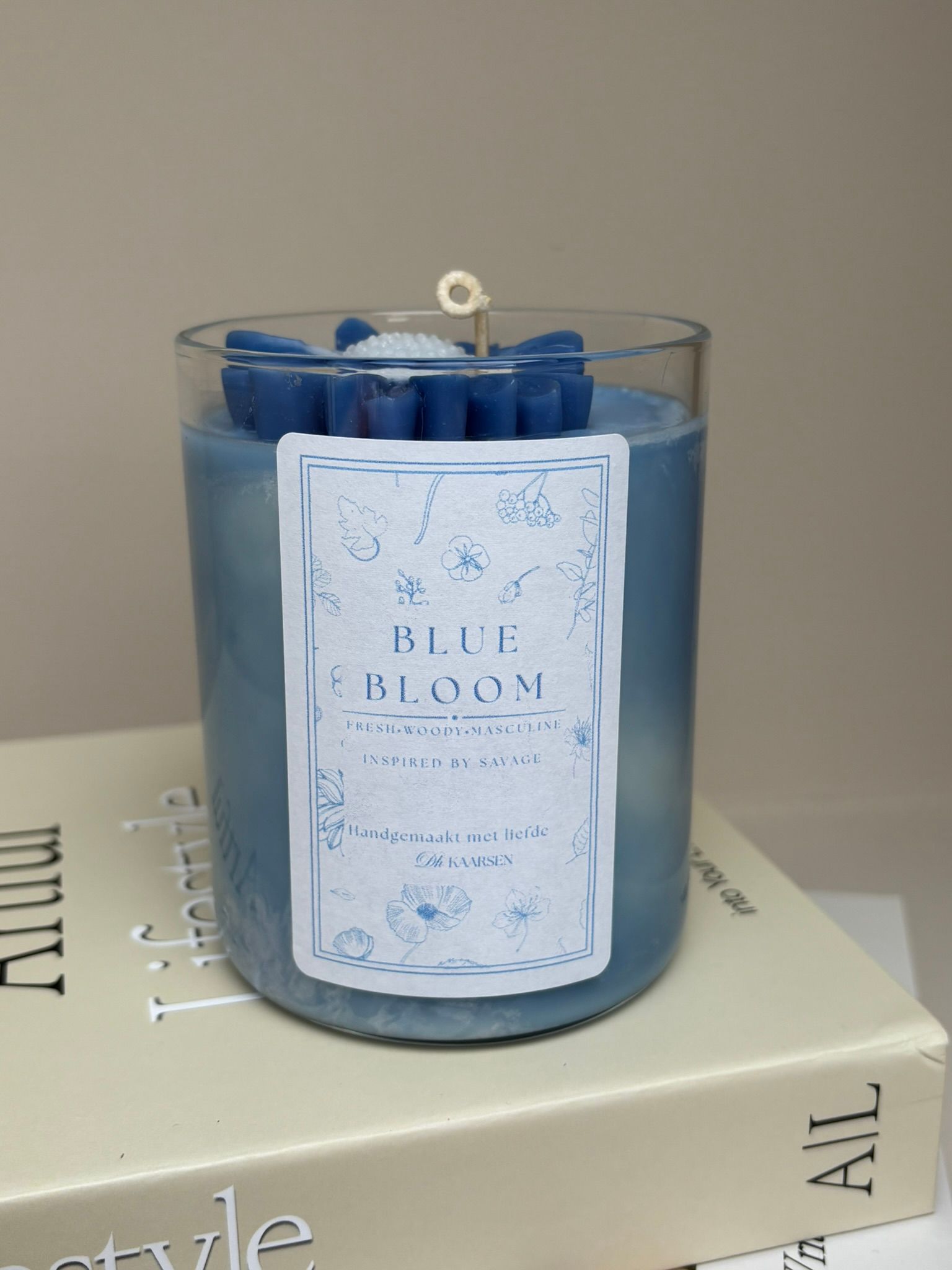 Een blauwe, bloemvormige kaars in een doorzichtige glazen houder, die op een lichtgekleurd boek staat.