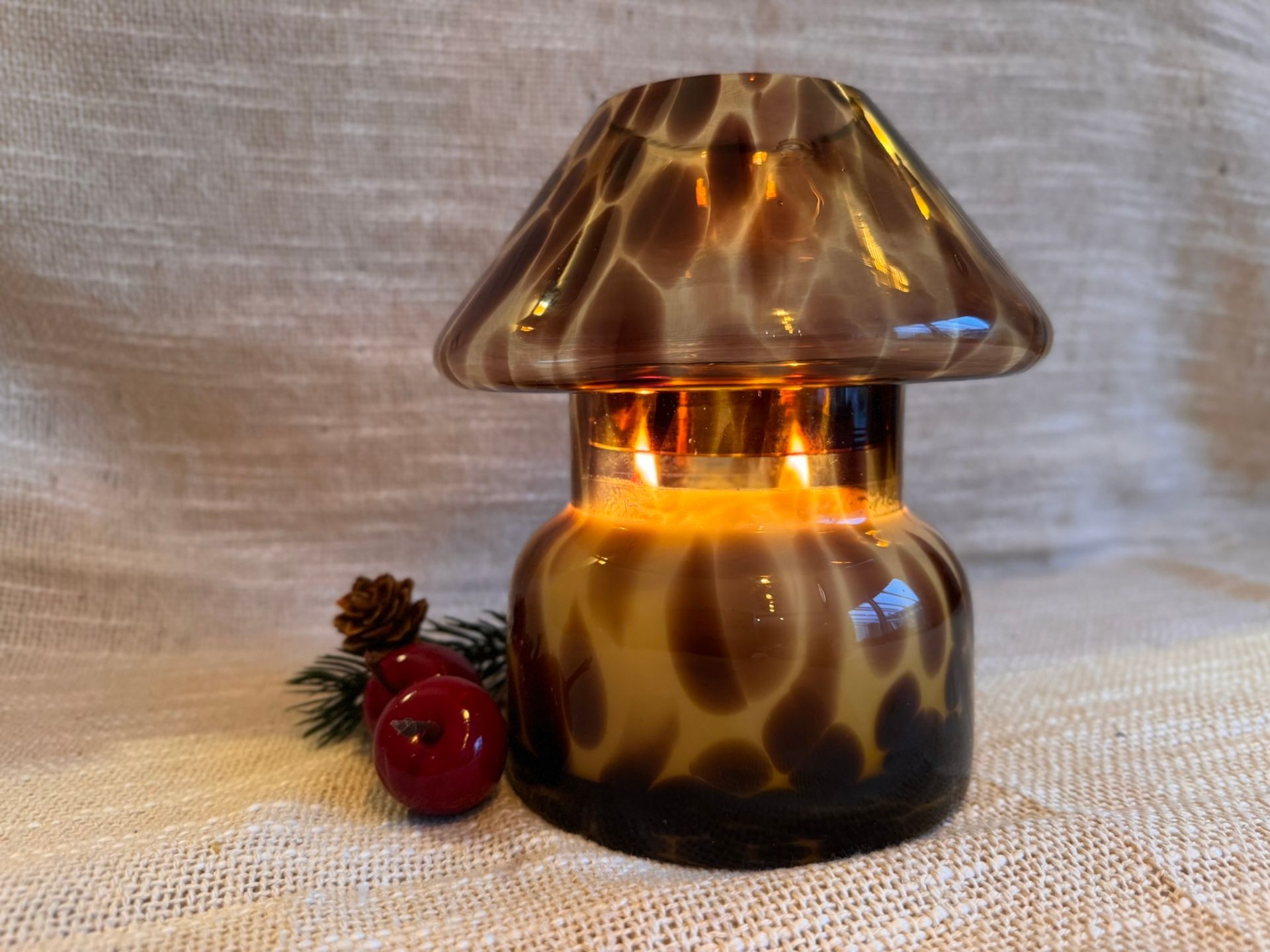 Kaarsenlamp, paddenstoelvormig, van amberkleurig glas, op een houten tafel met kerstversiering.