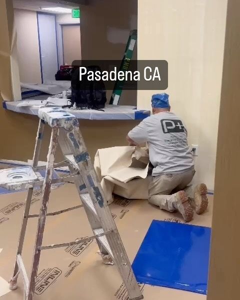A man kneeling down in a room with a ladder and a sign that says pasadena ca