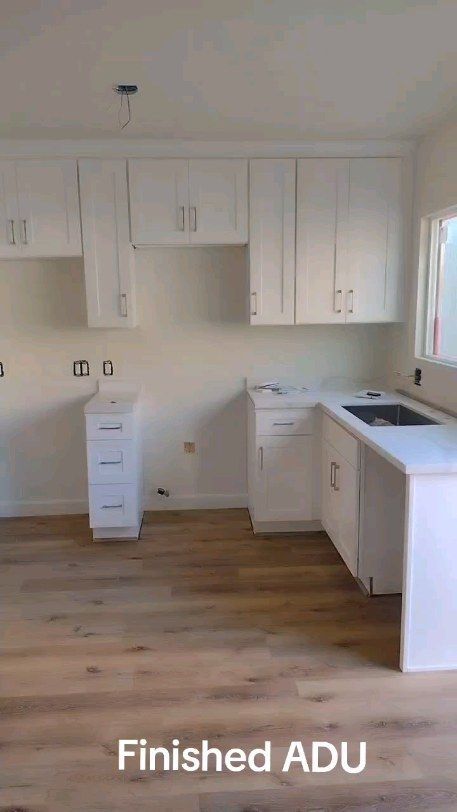 An empty kitchen with white cabinets and wooden floors.
