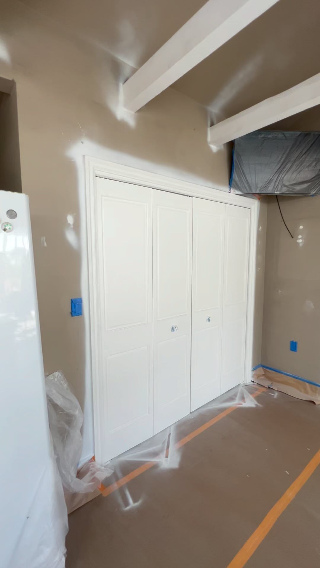 A room with white cabinets and a white refrigerator is being painted.