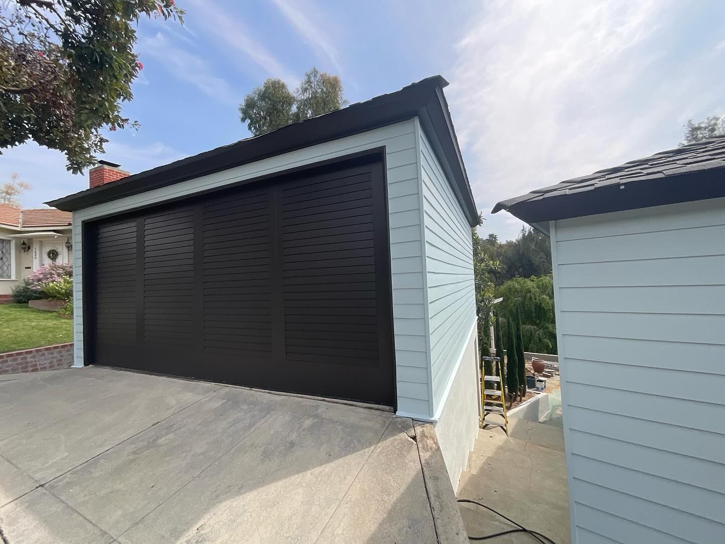 A garage with a black door is next to a house.