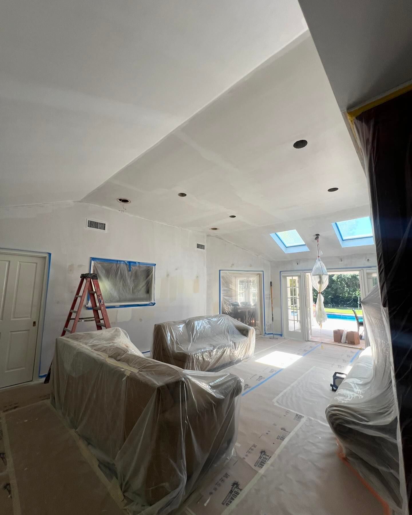 A living room with a couch covered in plastic and a ladder.