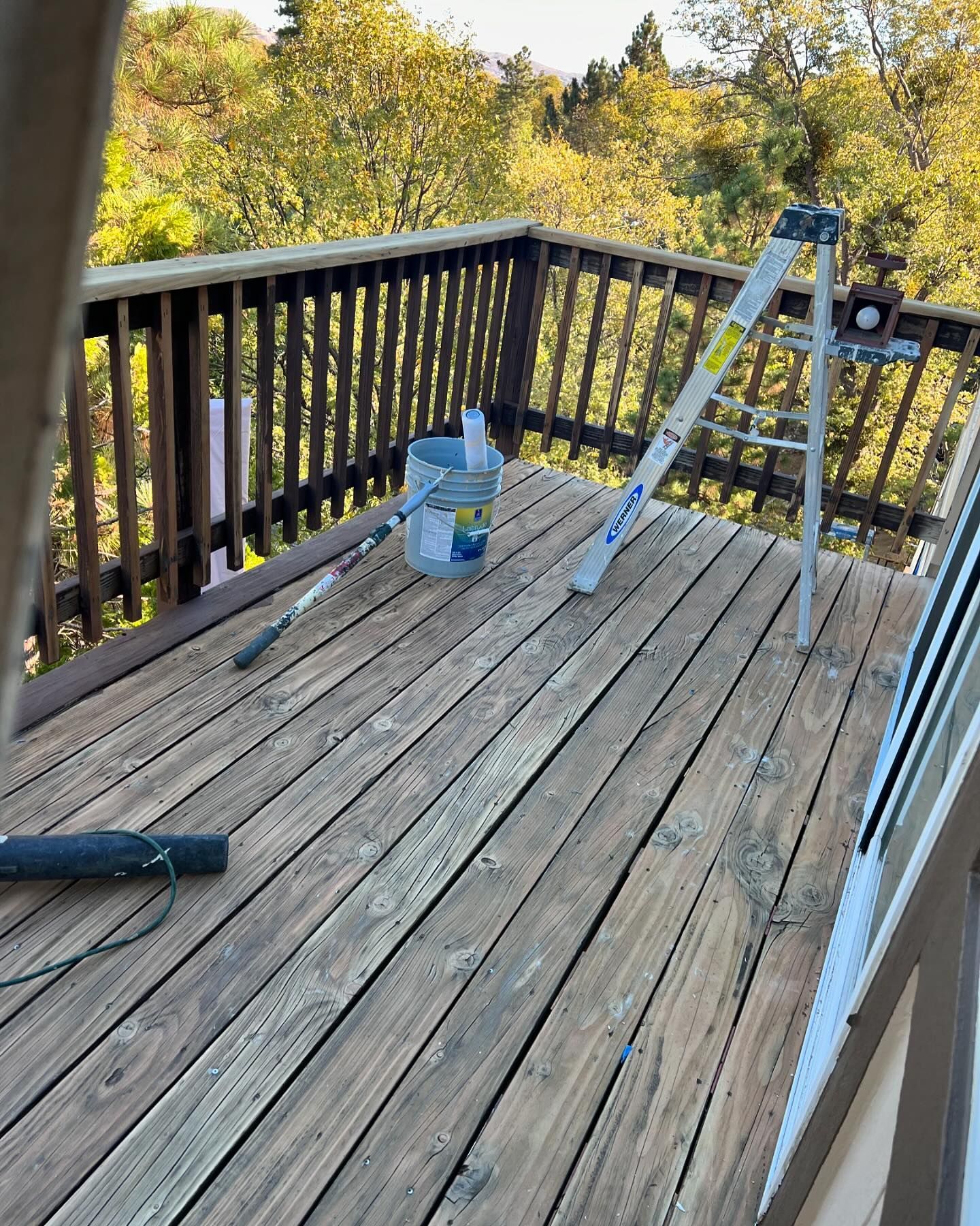 A wooden deck with a ladder and a bucket of paint on it.