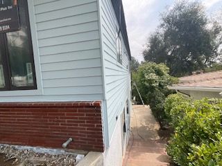 The side of a house with a brick wall and a white siding.