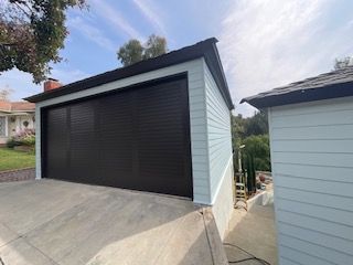 A garage with a black garage door is next to a shed.