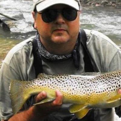 A man is holding a large brown trout in his hands.