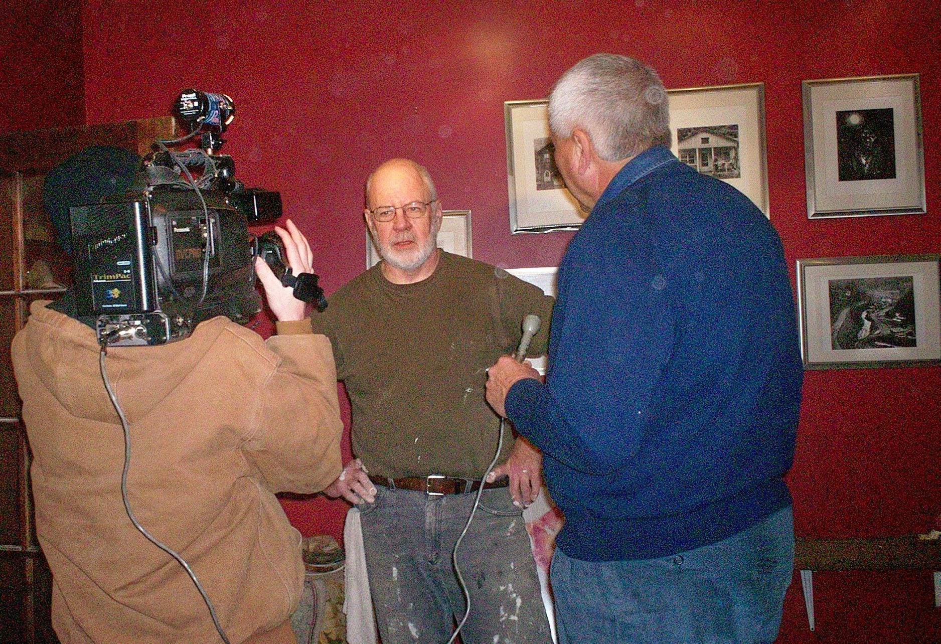 A man is being interviewed by a cameraman in front of a red wall