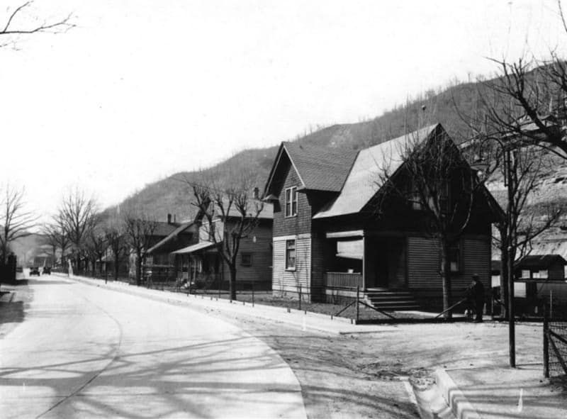 A black and white photo of a row of houses on the side of a road.