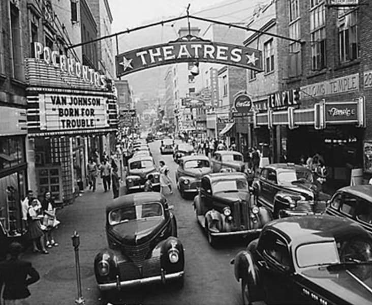 A black and white photo of a busy street with a sign that says theatres