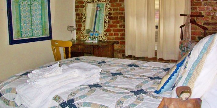 A bedroom with a bed , chair , mirror and a brick wall.