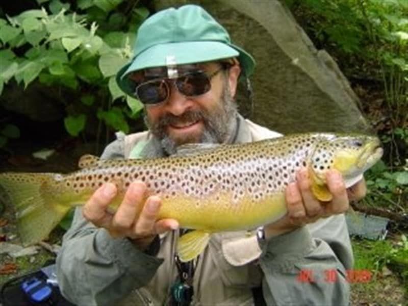 A man in a green hat is holding a brown trout