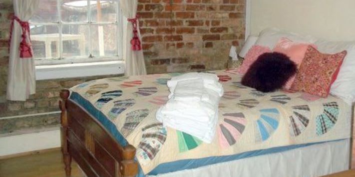 A bed with a quilt and pillows in a bedroom with a brick wall.