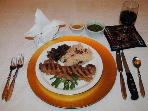 A plate of food on a gold plate with silverware and a glass of wine