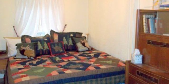 A bed with a quilt and pillows in a bedroom next to a window.