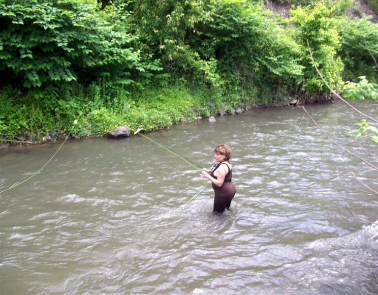 A woman in a wet suit is fishing in a river