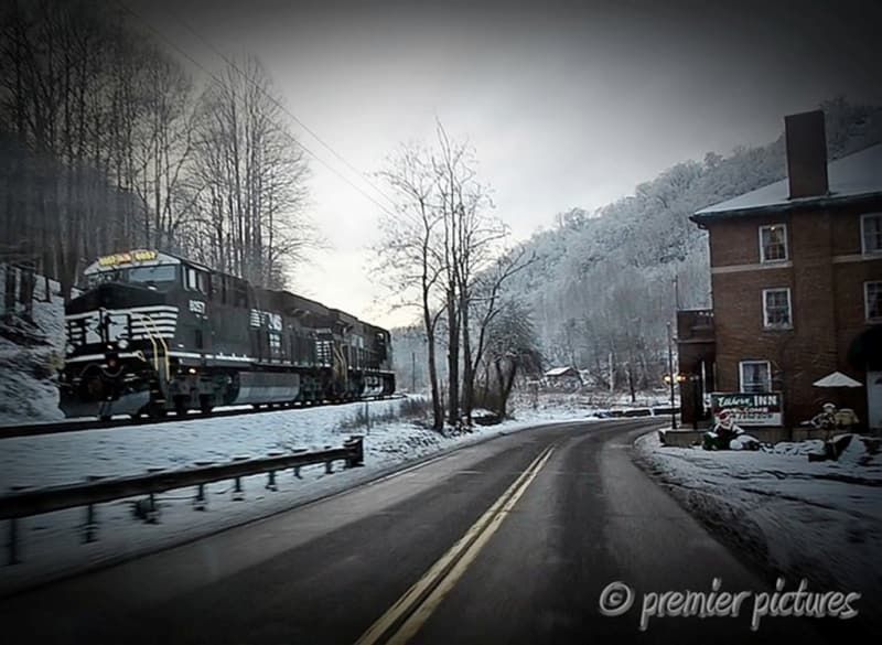 A train is going down a snowy road next to a brick building
