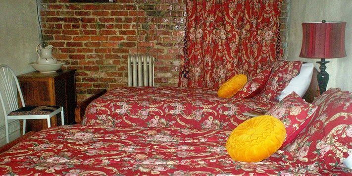 A bedroom with two beds , a lamp and a brick wall.